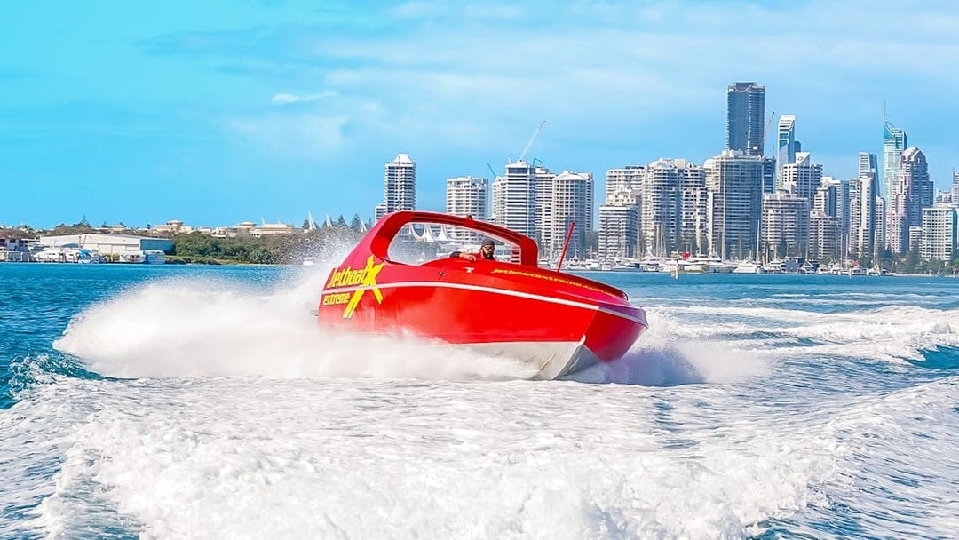 Jet boat speeding on water with city skyline in the background, Ultimate Jet Boat Ride.