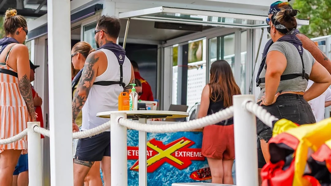 People preparing for the Ultimate Jet Boat Ride at a waterfront kiosk.