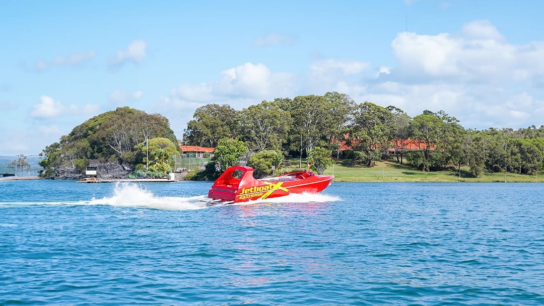 Red jet boat speeding on a blue river with green trees in the background.