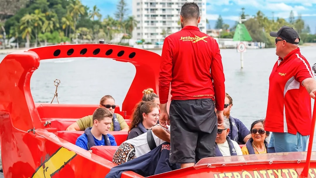 Group preparing for jet boat ride on a river, guided by instructors in red shirts.