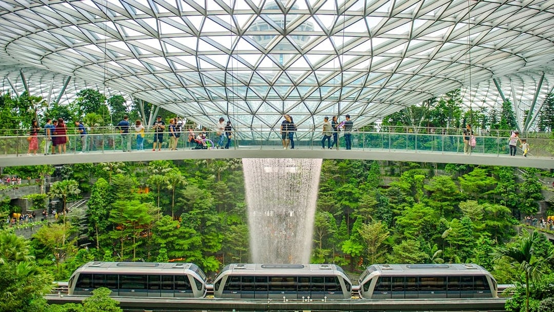 Canopy Bridge at Jewel Changi with waterfall and train below.