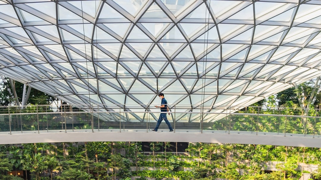 Man walking on Canopy Bridge at Jewel Changi Airport, Singapore, surrounded by lush greenery.
