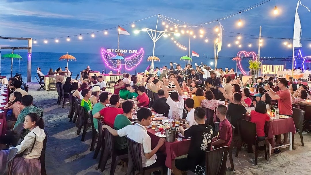 Crowded beachfront dining at New Dewata Cafe, Jimbaran Bali, with seafood dishes and ocean view.