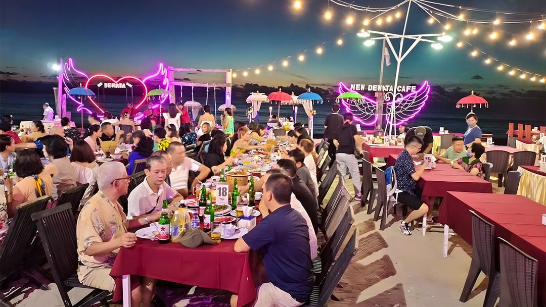 Dining at a beachfront seafood restaurant in Jimbaran, Bali with neon lights and ocean view.