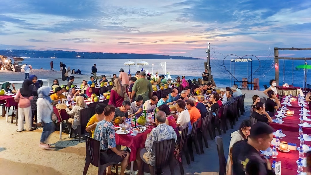 Group dining at sunset on Jimbaran Beach, Bali, with seafood and ocean view.