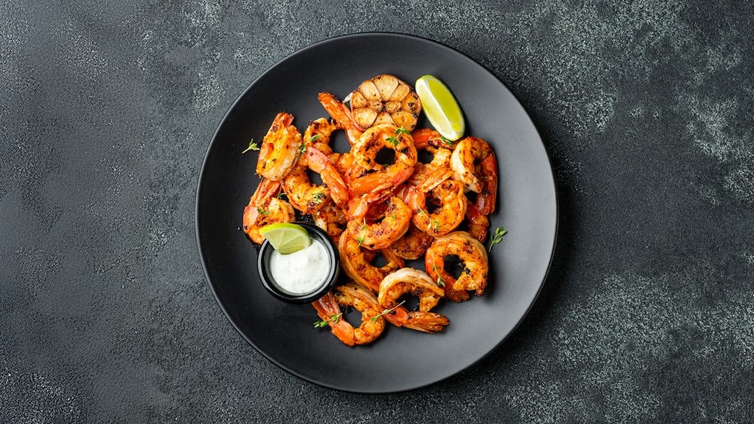 Grilled shrimp with lime and sauce on a black plate, Jimbaran Bali seafood dinner.
