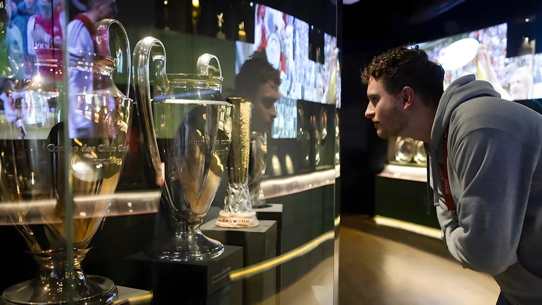 Visitor examining trophies at Johan Cruijff ArenA Classic Tour exhibit.