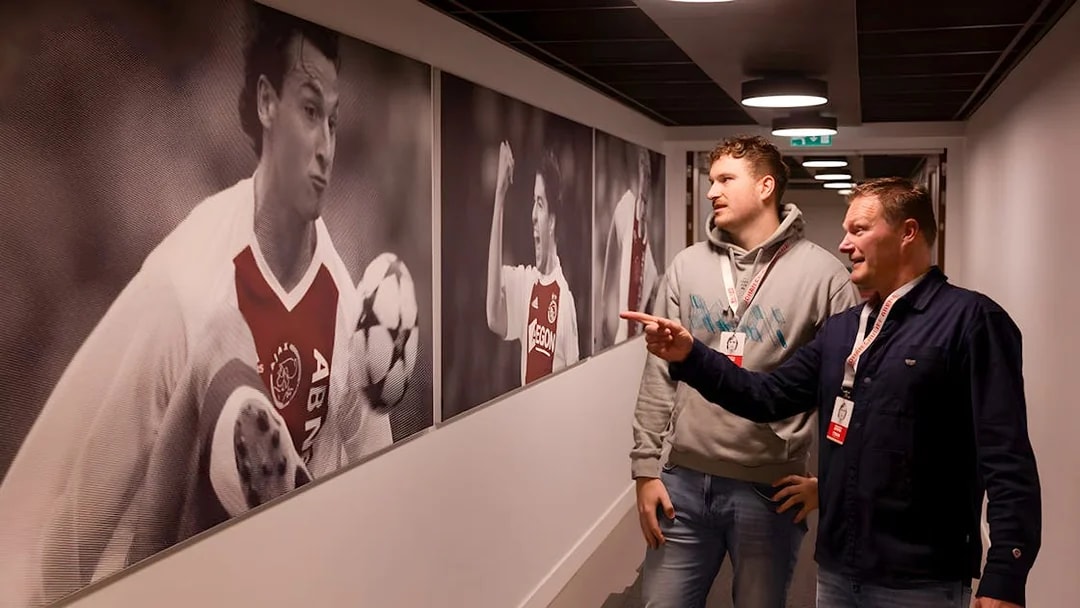 Visitors observing football player photos at Johan Cruijff ArenA tour.