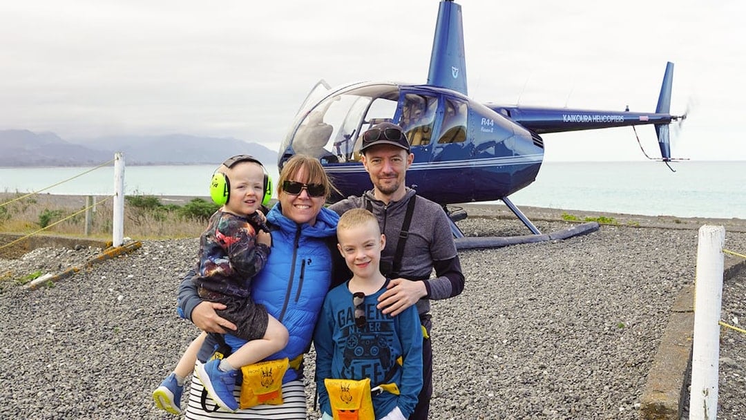 Family posing after helicopter ride in Kaikoura with ocean and mountains in background.