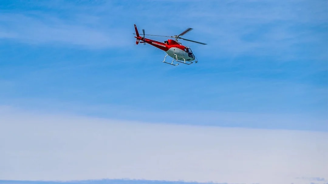 Helicopter flying over Kaikoura, New Zealand against a clear blue sky.