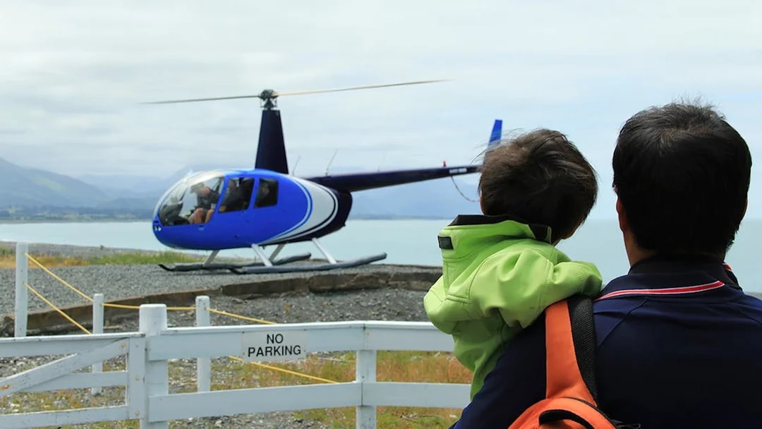 Father and son watching helicopter take off for whale watching in Kaikoura.