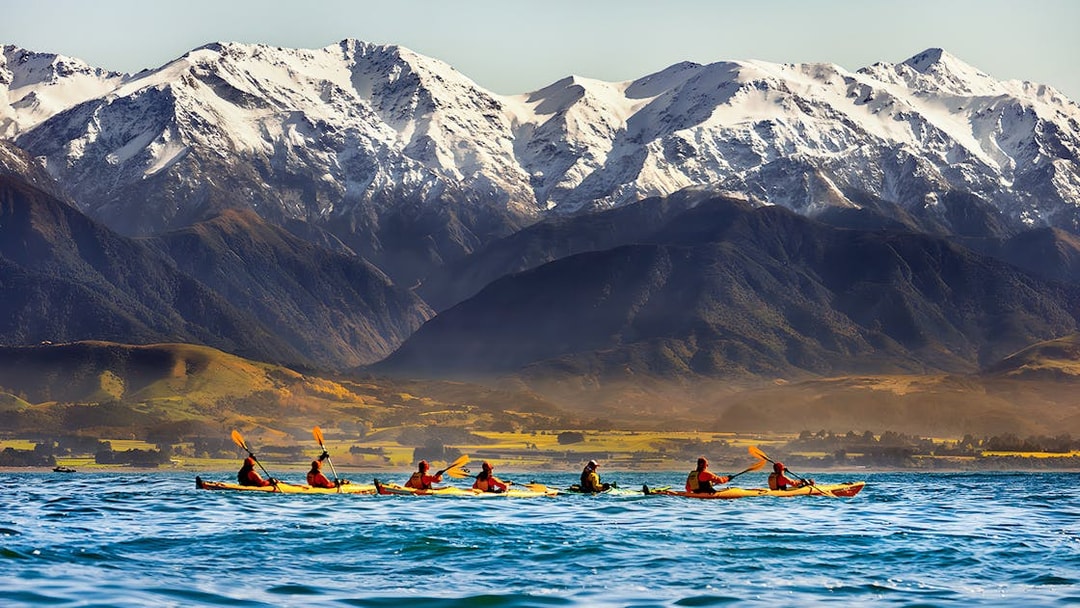 Kayakers paddling on a lake with snow-capped mountains in the background.