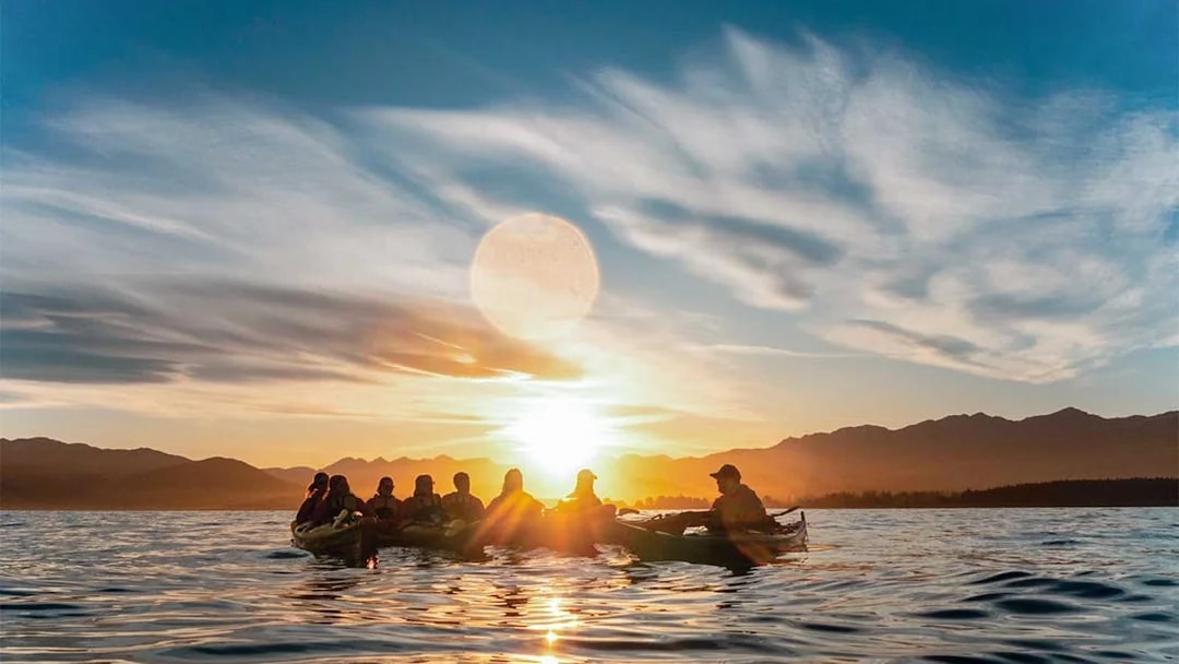 Kayakers paddling at sunset during a guided wildlife tour on a serene lake.