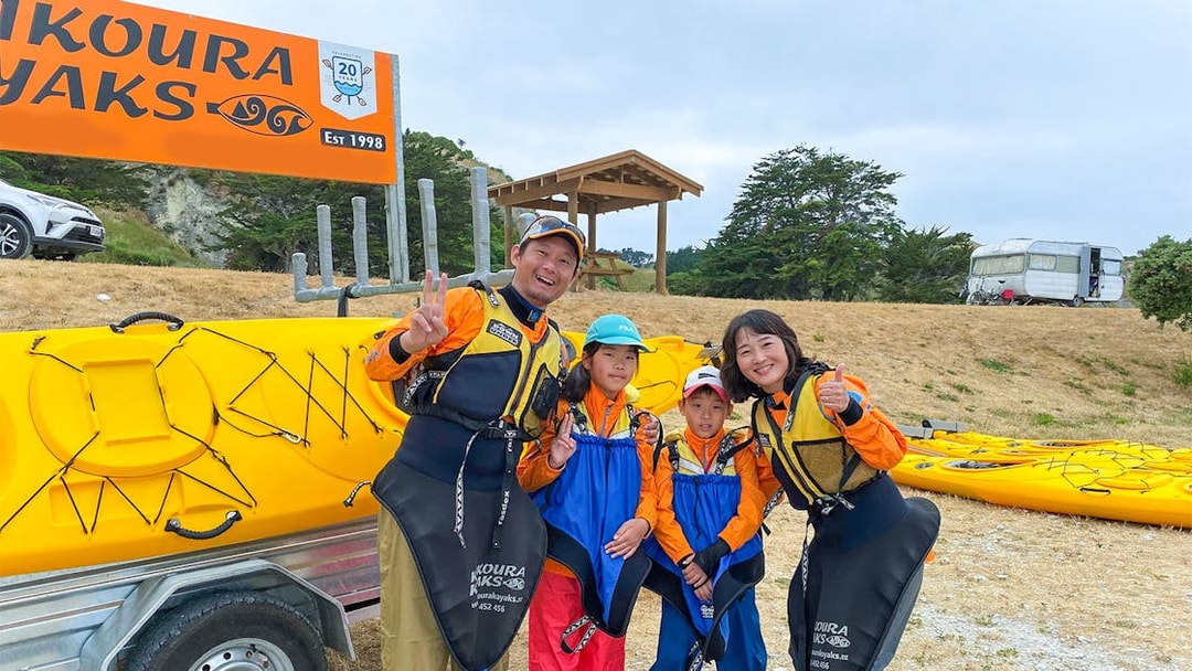 Family ready for kayaking adventure in Kaikoura, New Zealand, standing by yellow kayaks.