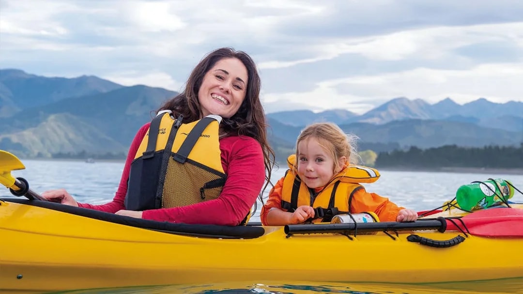 Mother and child kayaking on a lake with mountains in the background.