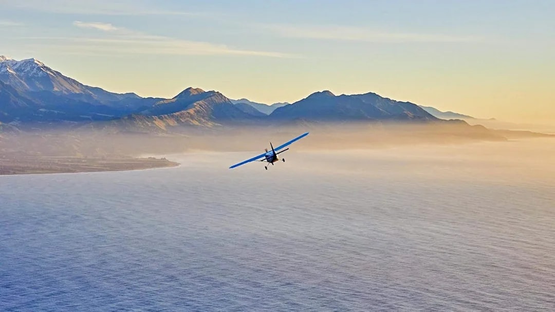 Airplane flying over Kaikoura coast during sunset.