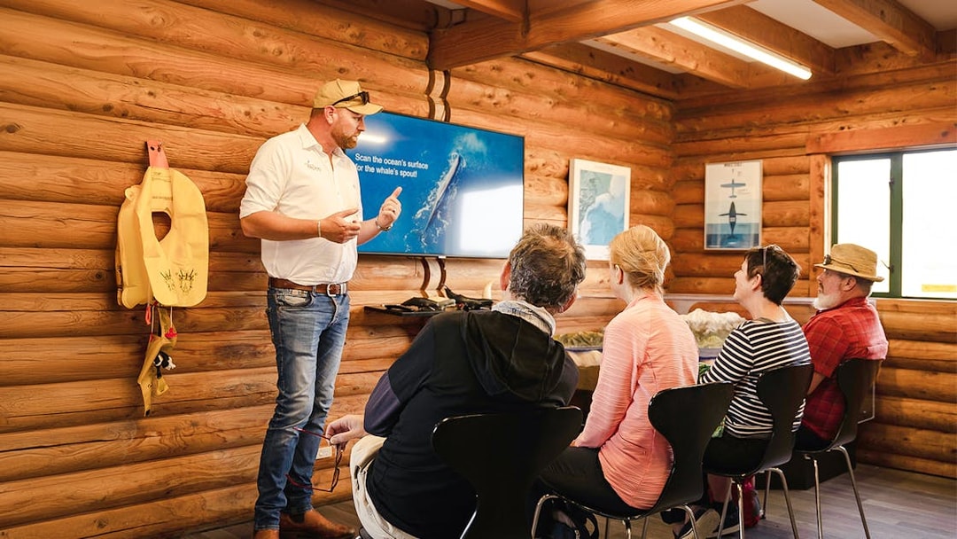Crew conducting pre-flight briefing in a wooden cabin with a screen presentation.