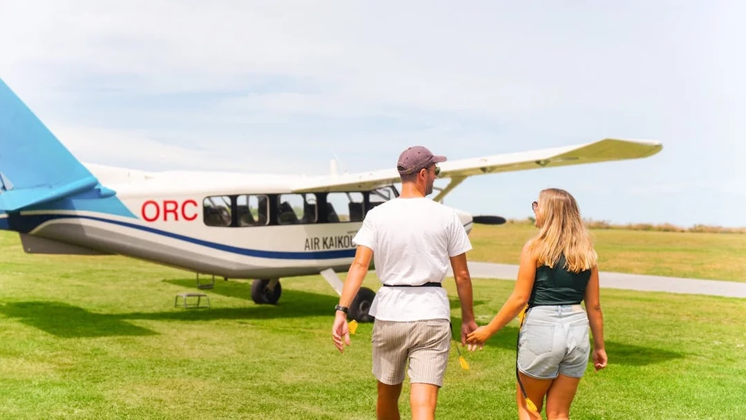 Couple walking towards Kaikoura flight on grassy airfield.