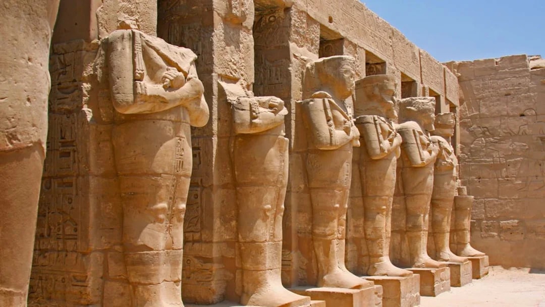 Row of ancient statues at Karnak Temple, Egypt, under a clear sky.