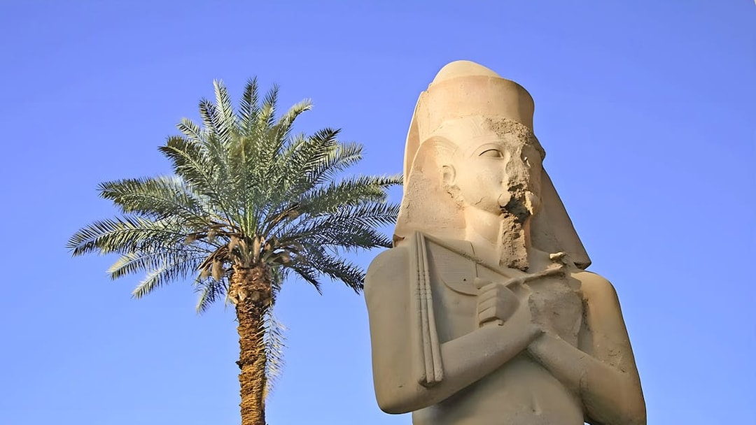 Statue of ancient Egyptian pharaoh at Karnak Temple with palm tree, Luxor, Egypt.