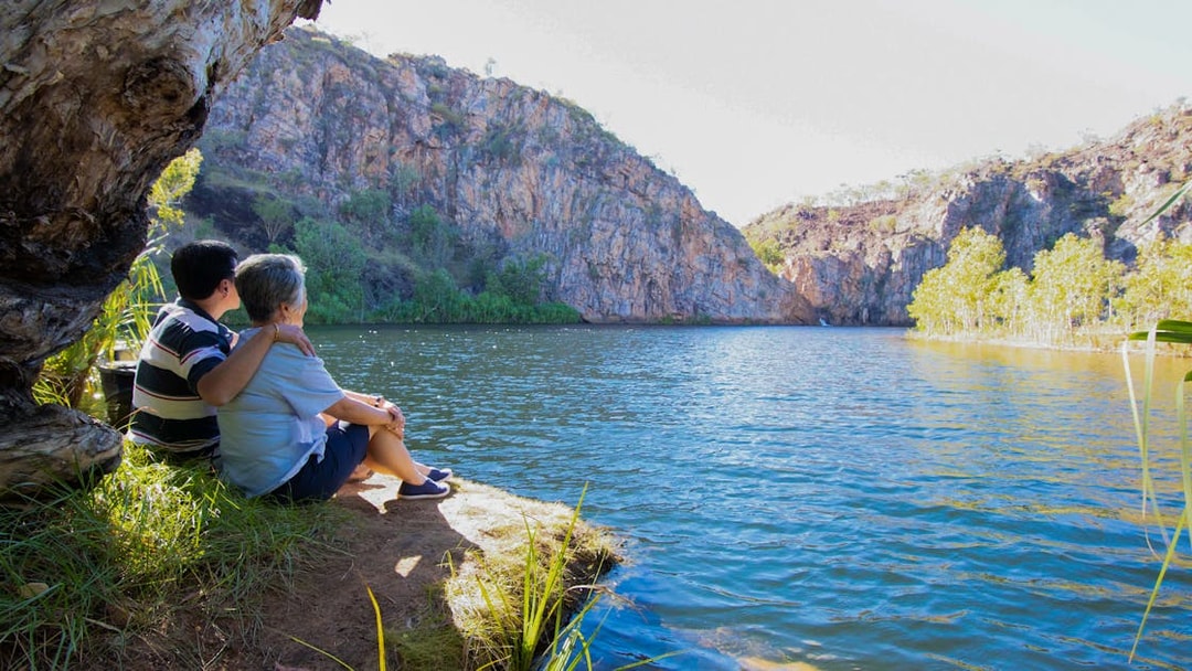 Couple sitting by Katherine Gorge, enjoying the view of cliffs and water during a guided tour.