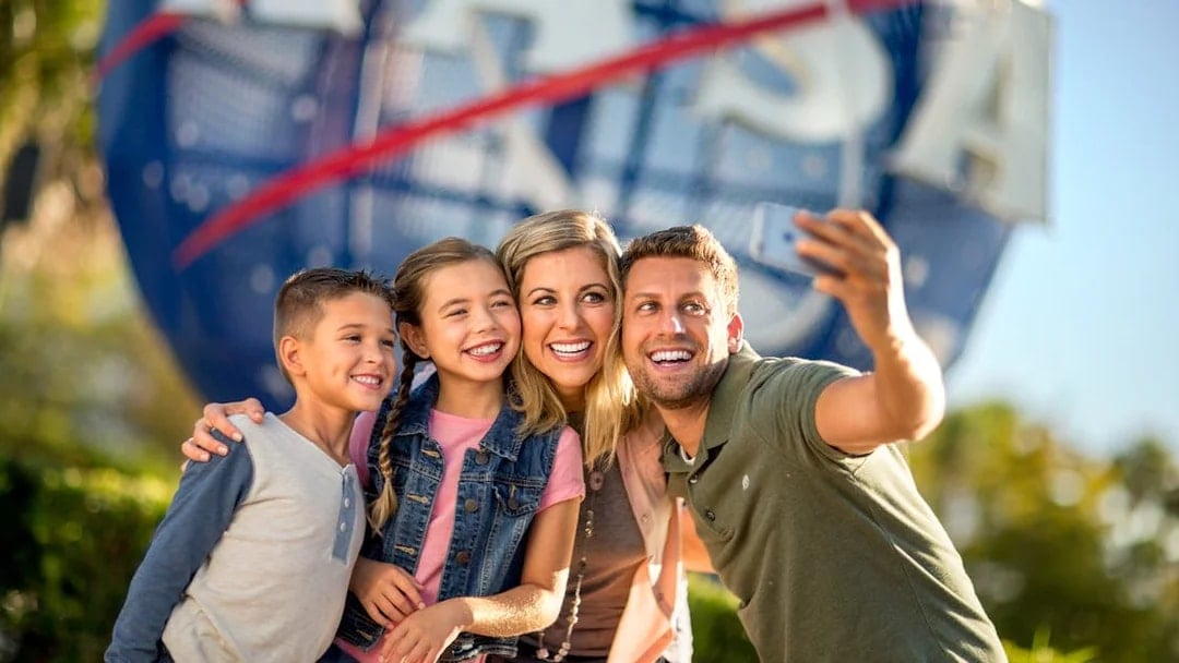 Family taking a selfie at Kennedy Space Center with NASA globe in background.