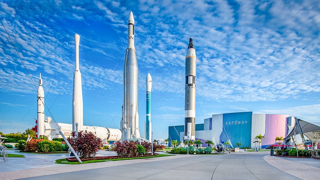 Kennedy Space Center facade with rockets on display under a blue sky.
