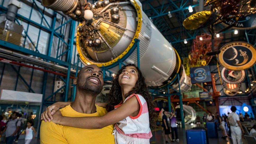 Father and daughter admiring a Saturn V rocket at Kennedy Space Center.