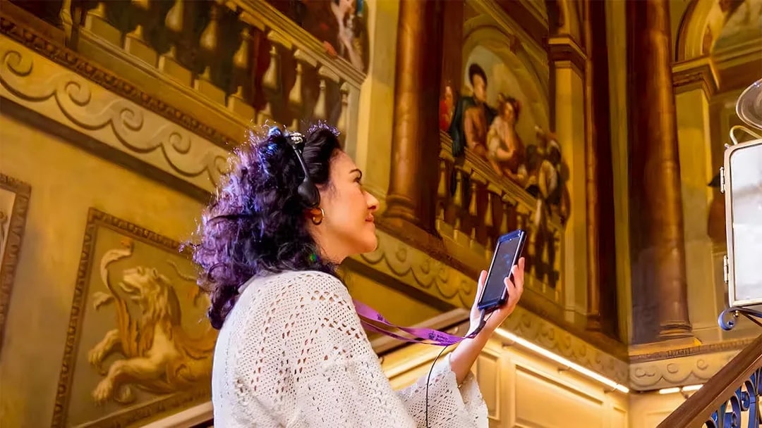 Visitor using audio guide at Kensington Palace staircase.