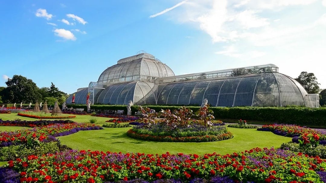Kew Gardens Palm House with vibrant flower beds in London.