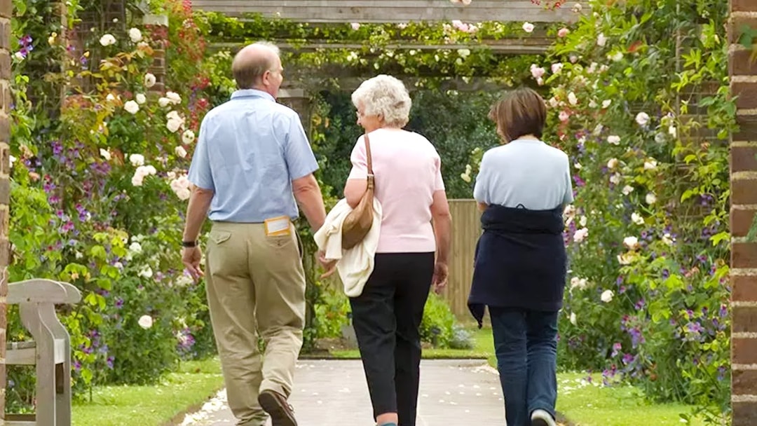 Visitors walking through a flower-covered archway at Kew Gardens.