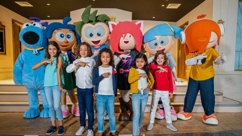 Children posing with Kidzania Dubai mascots indoors.