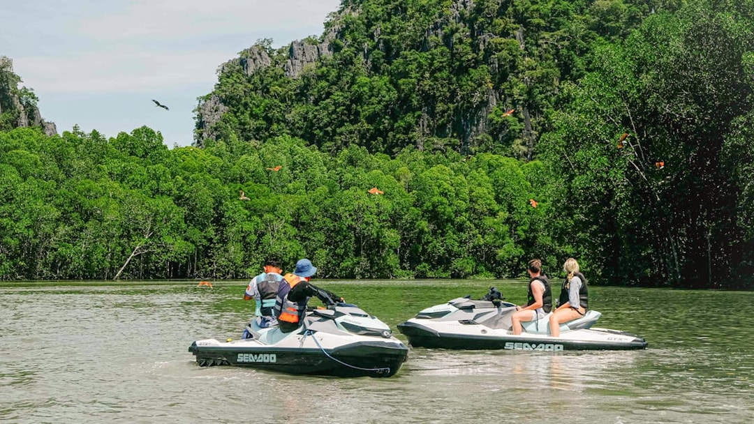 Jet skis on Langkawi's Kilim Geopark waters with lush greenery and limestone cliffs.