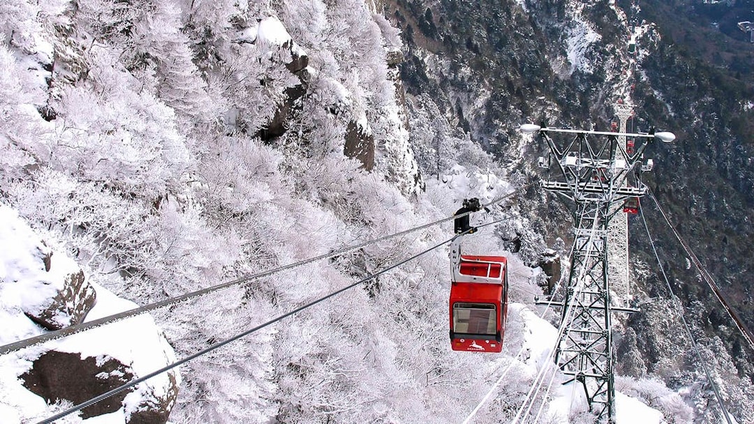 Red cable car ascending snowy mountain with Kintetsu Rail Pass.