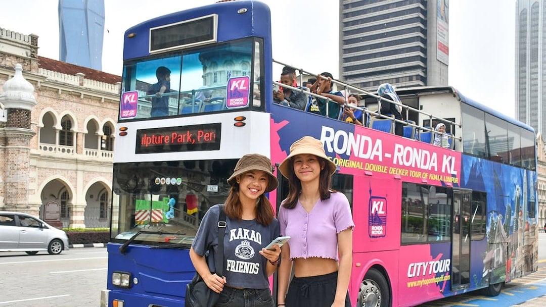 Hop-On Hop-Off bus tour in Kuala Lumpur with passengers and city landmarks in the background.