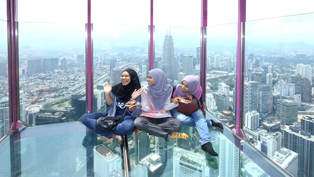 Female tourists sitting on KL Tower observation deck with city view.