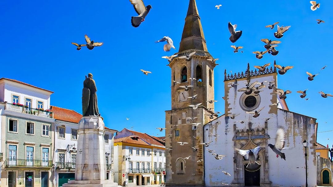 Historic church and statue in Tomar, Portugal, with pigeons flying, part of Knights Templar Tour from Lisbon.