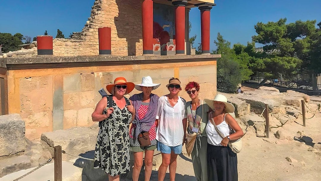 Guests exploring Knossos Palace ruins with frescoes and columns in Crete.
