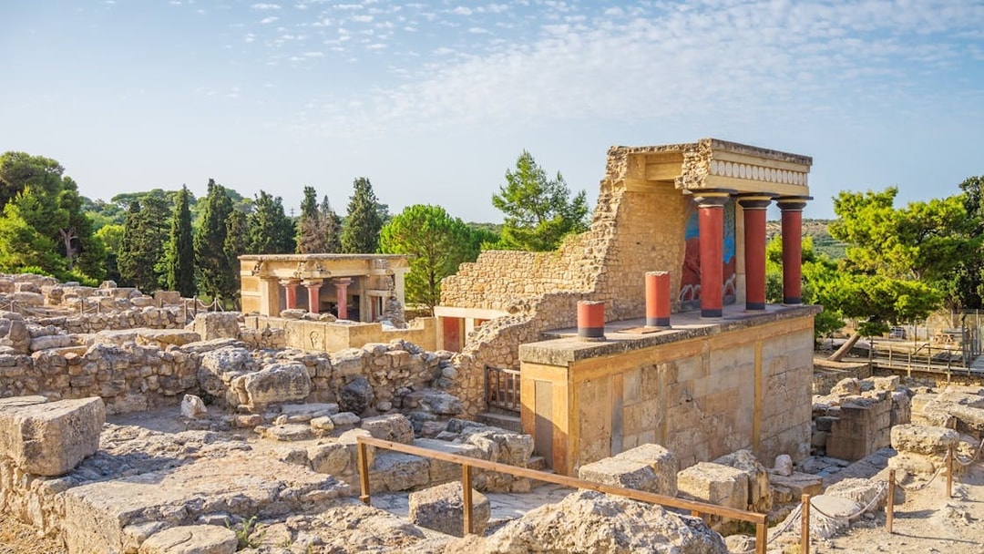 Knossos Palace ruins with red columns and ancient stone structures in Crete, Greece.