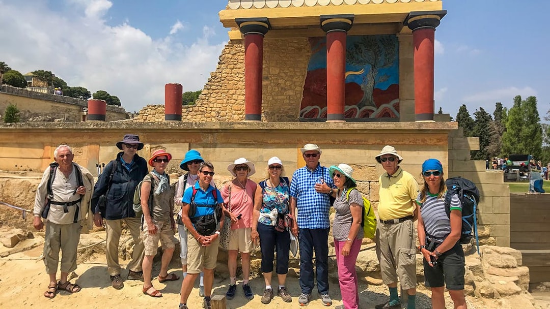 Group of tourists at Knossos Palace, Crete, with ancient ruins and fresco in the background.