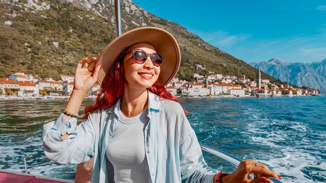 Female guest on a boat trip in Kotor Bay with coastal town view.