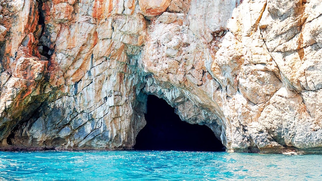 Blue cave entrance in Kotor Bay with rocky cliffs and turquoise water.