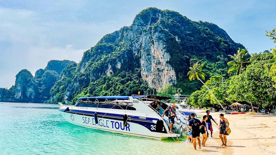 Boat tour arriving at Phi Phi Islands beach with limestone cliffs in the background.