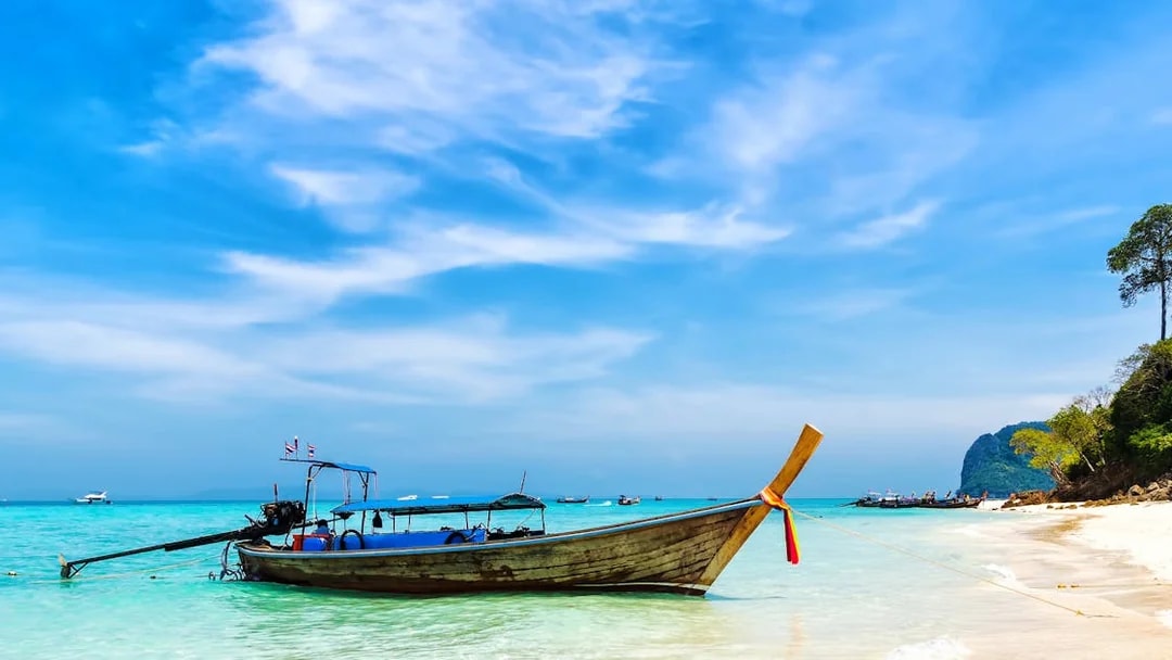 Longtail boat on a sandy beach with clear turquoise water in Thailand.