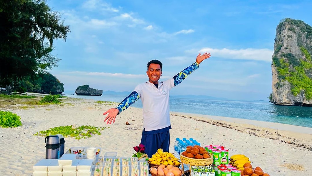 Buffet lunch setup on Phi Phi Don beach with a smiling host and scenic ocean view.