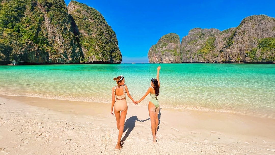 Women walking on Maya Beach, Krabi, with limestone cliffs in the background.