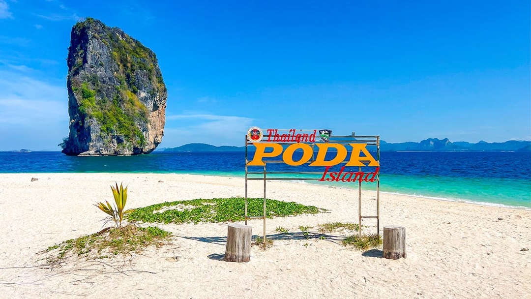Poda Island sign on sandy beach with limestone rock in Thailand.