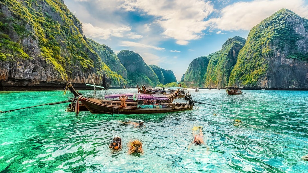 Snorkelers exploring clear waters at Maya Bay, Phi Phi Islands, Thailand with limestone cliffs.