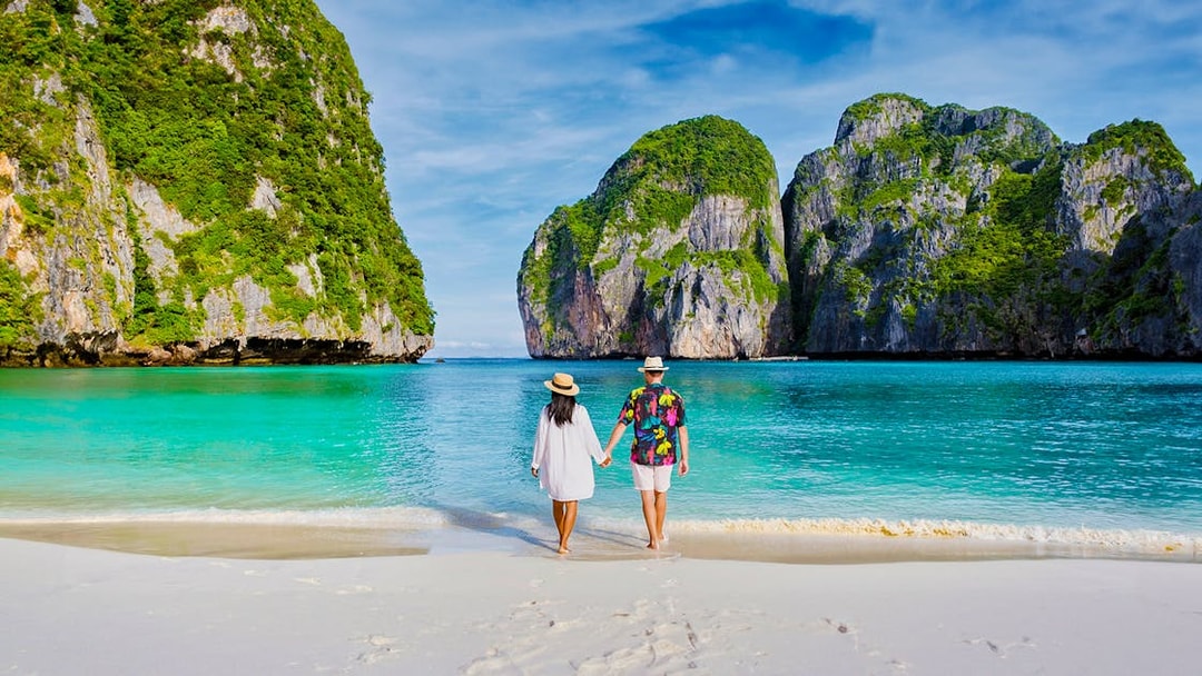 Couple walking on beach towards longtail boat in Koh Phi Phi lagoon, Thailand.