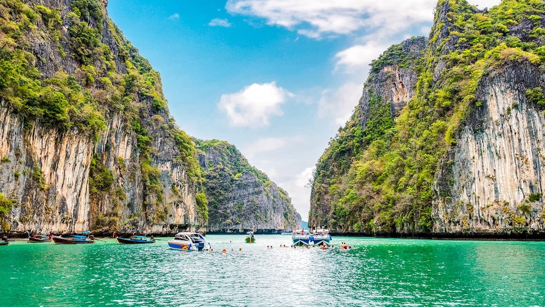 Boats and swimmers in Pileh Lagoon, surrounded by limestone cliffs, Krabi, Thailand.